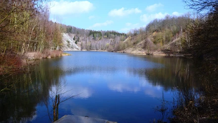 Finkenkuhle_HD_16zu9.JPG Ruhiger See in stillgelegtem Tagebau Finkenkuhle, umgeben von bewaldeten Hängen unter blauem Himmel.