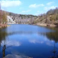 Finkenkuhle_HD_16zu9.JPG Ruhiger See in stillgelegtem Tagebau Finkenkuhle, umgeben von bewaldeten Hängen unter blauem Himmel.