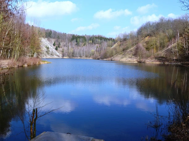 Finkenkuhle_HD_16zu9.JPG Ruhiger See in stillgelegtem Tagebau Finkenkuhle, umgeben von bewaldeten Hängen unter blauem Himmel.