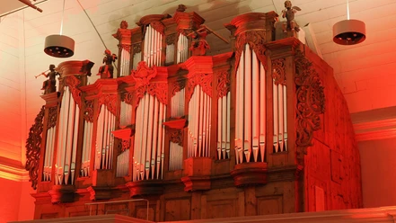 Historische Holzorgel mit weißen Pfeifen, Schnitzwerk und roter Beleuchtung.
