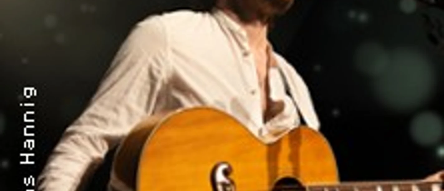 Musiker mit Akustikgitarre auf einer beleuchteten Bühne während eines Auftritts