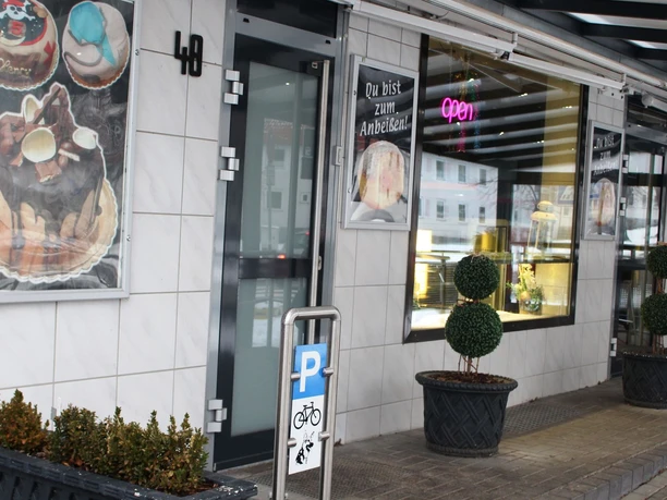 Bäckerei Conti_HD_16zu9.JPG Eingangsbereich der Bäckerei Conti mit Schaufenstern, Tortenwerbung und Topfpflanzen.