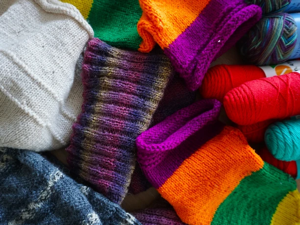 Stikke-Kaffee - Wolle u Projekte.JPG Bunte Wollknäuel und handgestrickte Textilien in verschiedenen Farben liegen nah beieinander.