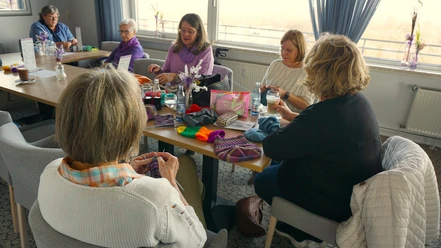 Strikke-Kaffe - Teilnehmerinnen am Tisch.JPG Mehrere Frauen sitzen an einem Tisch, stricken bunte Wolle und trinken Kaffee.