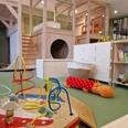 Kids Safari Leipzig - Leipzig mit Kindern Im Vordergrund ist ein Spieltisch mit Motorikschleife zu erkennen, im Hintergrund ein Würfelregal mit Büchern und anderem Spielzeug sowie ein zweistöckiger Indoor-Spielplatz mit Treppe und Schaukel