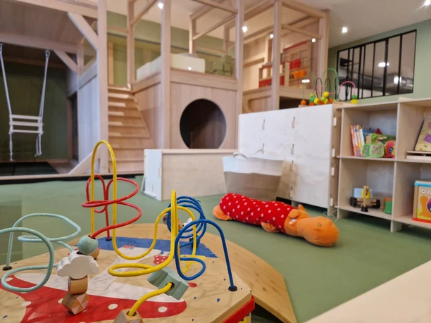 Kids Safari Leipzig - Leipzig mit Kindern Im Vordergrund ist ein Spieltisch mit Motorikschleife zu erkennen, im Hintergrund ein Würfelregal mit Büchern und anderem Spielzeug sowie ein zweistöckiger Indoor-Spielplatz mit Treppe und Schaukel