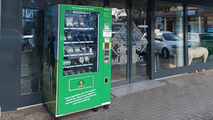 Regiomat_Münnig_HD_16zu9.jpg Grüner Verkaufsautomat mit regionalen Fleischprodukten vor dem Schaufenster einer Fleischerei.
