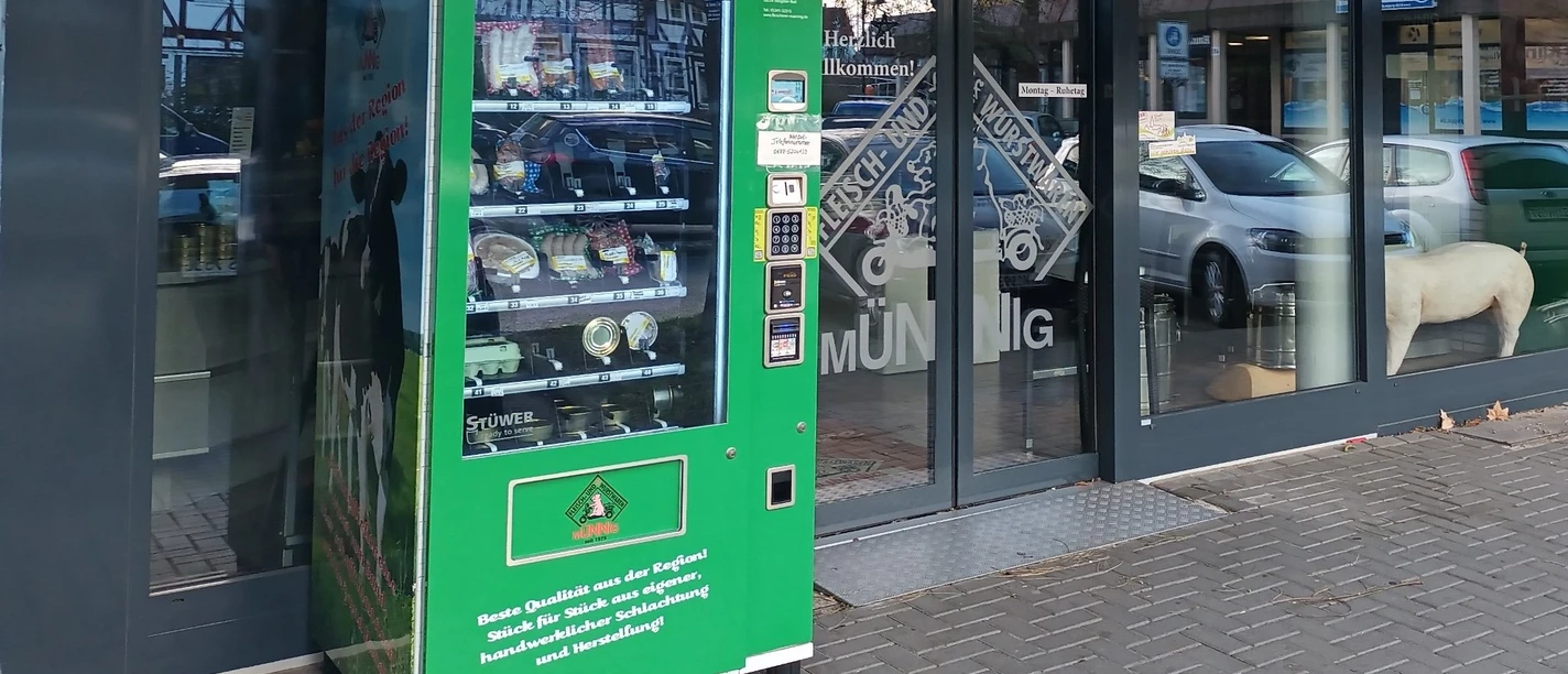 Regiomat_Münnig_HD_16zu9.jpg Grüner Verkaufsautomat mit regionalen Fleischprodukten vor dem Schaufenster einer Fleischerei.