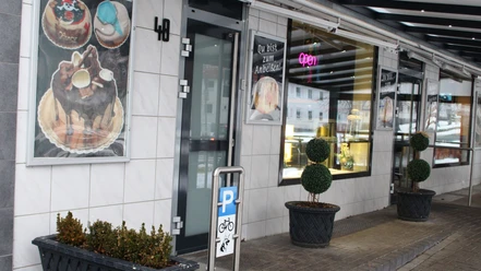 Eingang zur Bäckerei Conti in Salzgitter-Bad Eingangsbereich der Bäckerei Conti mit großen Fenstern, Plakaten und Pflanzenkübeln vor der Tür.