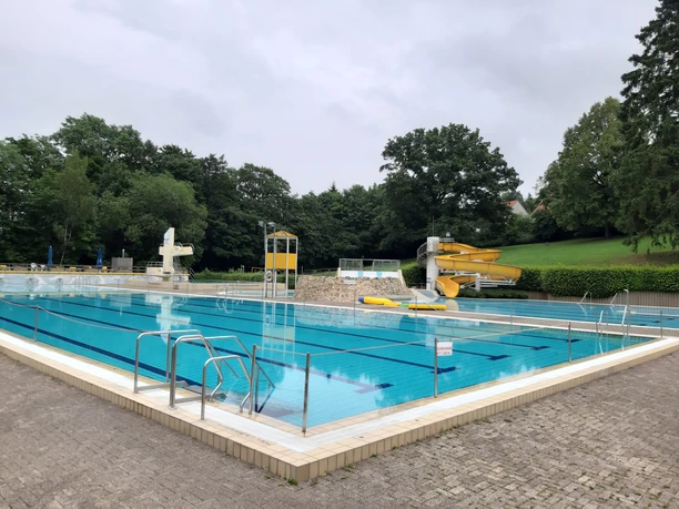 Sportbecken im Freizeitbad mit Schwimmbahnen, Sprungturm und gelber Rutsche im Außenbereich
