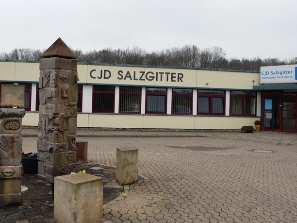 Flaches Gebäude des CJD Salzgitter mit gepflastertem Vorplatz und verzierten Steinsäulen.