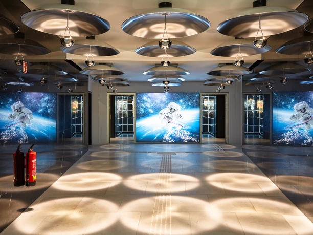 Futuristically illuminated hotel lobby with round ceiling lights and large astronaut motifs.