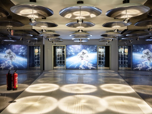 25hours Hotel The Circle Lobby Futuristisch beleuchtete Hotellobby mit runden Deckenleuchten und großen Astronautenmotiven.