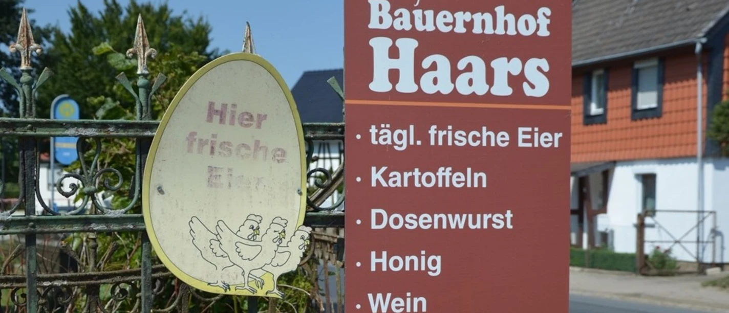 Ein braunes Schild vor einem Hoftor bewirbt frische Eier, Kartoffeln und Honig vom Bauernhof Haars.