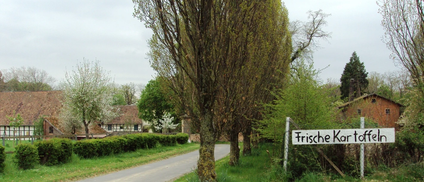 Hofladen_Nienrode_HD_16zu9.JPG Zufahrt zu Fachwerkhäusern. Ein Schild am Wegrand bewirbt frische Kartoffeln.