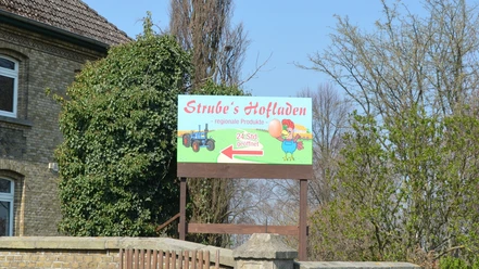 Schild von Strube's Hofladen bewirbt 24-Stunden-Verkauf regionaler Produkte am Backsteinhaus.