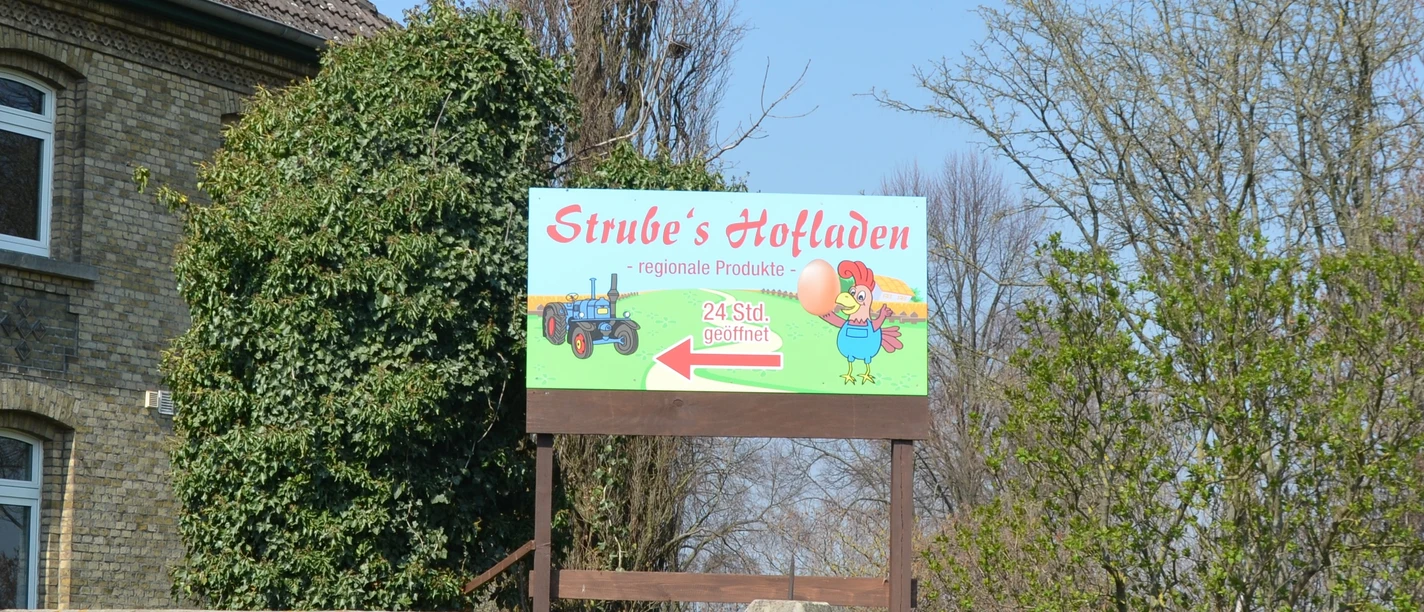 Schild von Strube's Hofladen bewirbt 24-Stunden-Verkauf regionaler Produkte am Backsteinhaus.