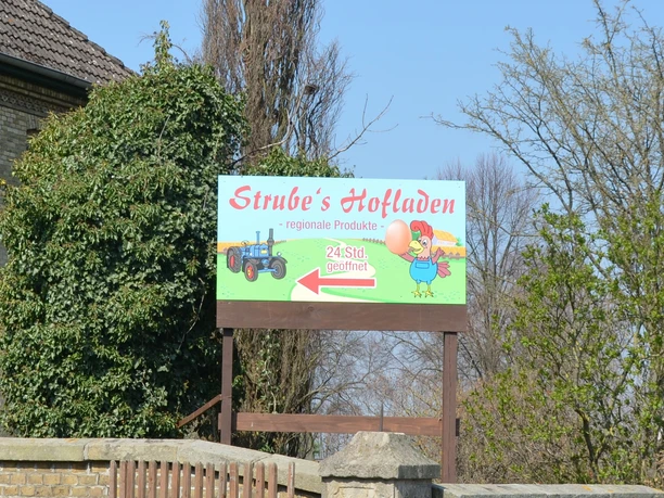 Schild von Strube's Hofladen bewirbt 24-Stunden-Verkauf regionaler Produkte am Backsteinhaus.
