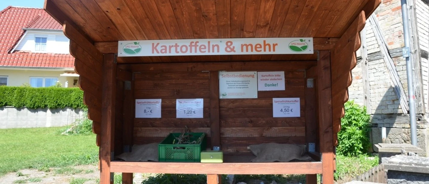 Hofstand_LPG_Heerte_HD_16zu9.JPG Ein hölzerner Verkaufsstand zur Selbstbedienung mit Schild Kartoffeln & mehr.