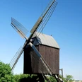 Mühle Lichtenberg_Anne König_HD_16zu9.jpg Historische Bockwindmühle aus Holz mit Flügeln vor blauem Himmel und grünen Bäumen.