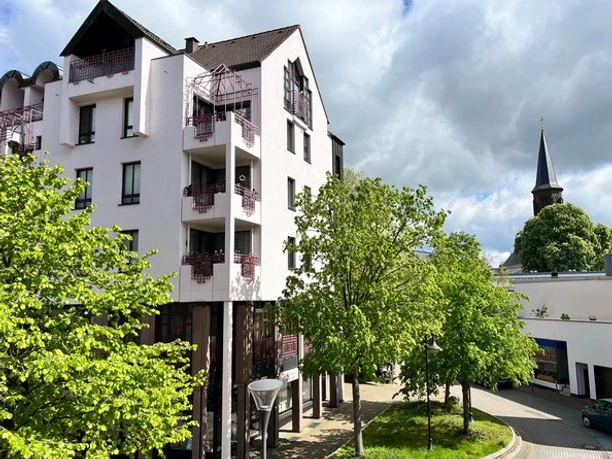 Außenansicht, Apartment - Der Gerber in Hilden Moderne Außenansicht des Apartment - Der Gerber in Hilden. Mehrere Bäume säumen den Gehweg, ein Kirchturm ragt im Hintergrund auf.