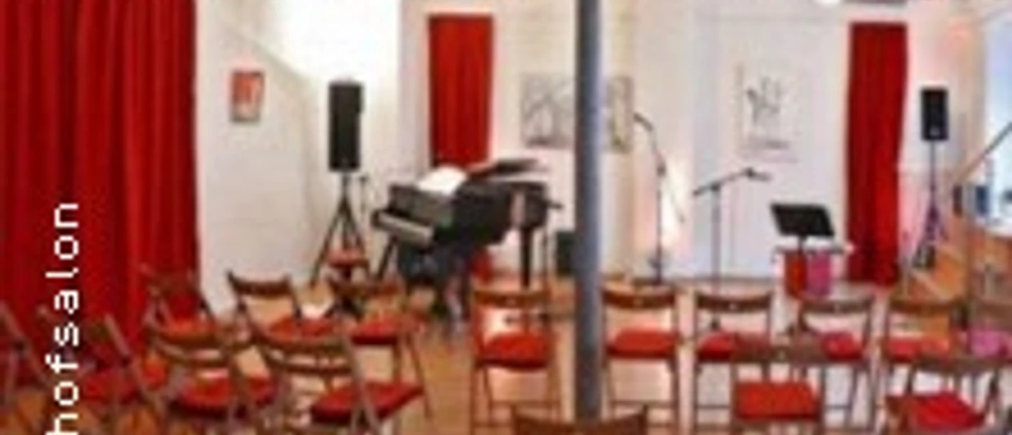 Kleiner Saal mit roten Vorhängen, Klavier und Stuhlreihen in heller Veranstaltungsumgebung