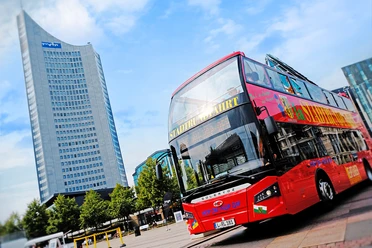 Tours de ville originaux à Leipzig - Expériences et tours à Leipzig Sur l'Augustusplatz se trouve un bus rouge à deux étages de la société Original Leipziger Stadtrundfahrten, avec en arrière-plan la tour City.
