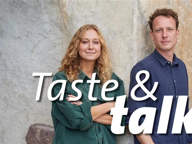 Taste & Talk im Kölner Weinkeller x Alois Lageder Zwei Personen vor einer Wand mit großem Taste & Talk Schriftzug.