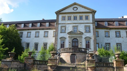 Frontansicht des weißen Schlosses Ringelheim mit Steintreppe und zentralem Rundbogenportal.