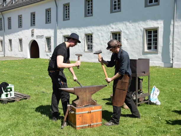 Altenberger Klostermarkt 2025 Zwei Schmied:innen bearbeiten Metall am Amboss vor dem Altenberger Dom auf dem Klostermarkt.