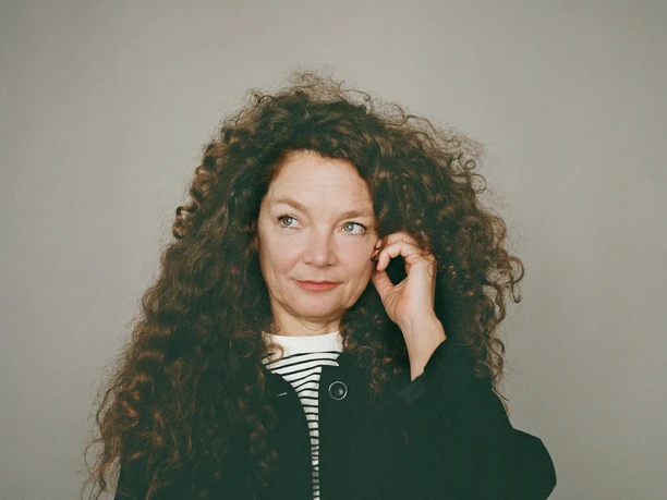 Stephanie Thiersch Person with long curly hair looking to the side against a neutral background.