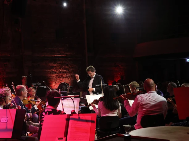 Philharmonisches Orchester Bhv im Apollo_Foto Kristin Niemann_WEB.jpg Ein Dirigent leitet das Philharmonische Orchester bei einem Konzert im roten Bühnenlicht.