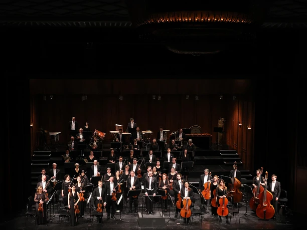 Philharmonisches Orchester 2023_1_Foto Kristin Niemann_WEB.jpg Das Philharmonische Orchester in Abendgarderobe auf einer beleuchteten Theaterbühne.