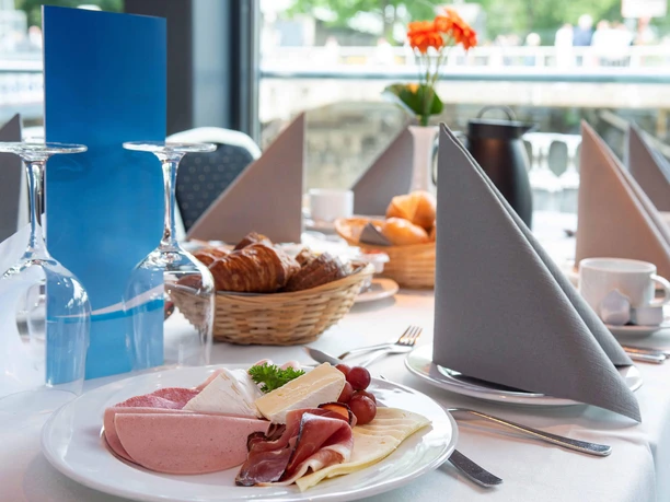 Sonntagsbrunch auf dem Rhein Festlich gedeckter Tisch mit Aufschnitt, Käse, Gebäckkörben und Blick durch große Fenster