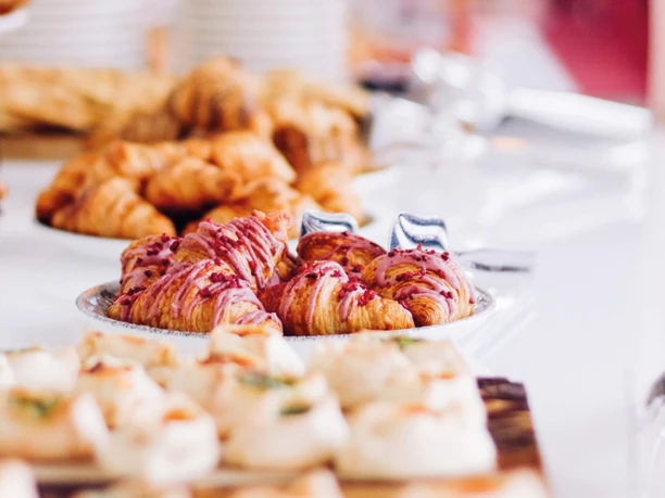 Sonntagsbrunch auf dem Rhein Croissants und Gebäck mit rosa Glasur auf einer Buffettafel in hellem Licht arrangiert