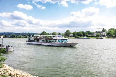 Linienfahrt auf dem Rhein Ein Ausflugsschiff fährt über den Rhein vor grünen Ufern und hellem Himmel