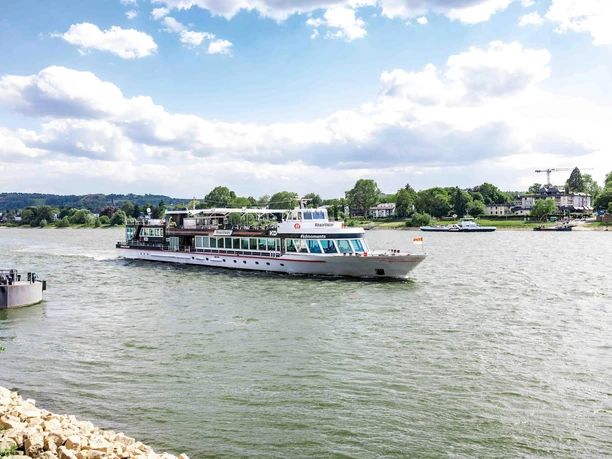 Scheduled trip on the Rhine An excursion boat sails across the Rhine against green banks and a bright sky