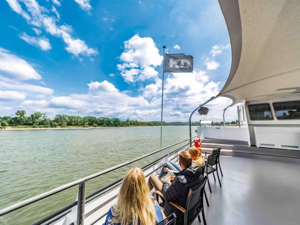 Linienfahrt auf dem Rhein Personen sitzen auf dem Außendeck eines KD-Schiffs und blicken über den Rhein.