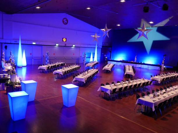 Stadthalle Offenbach - dekorierte Stadthalle Festlich dekorierte Stadthalle Offenbach mit blauem Galalicht, weiß gedeckten langen Tafeln, leuchtenden Dekoelementen und hängenden Sternen.