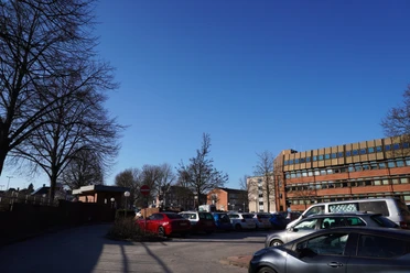 Parkplatz Polizei Lüneburg Geparkte Autos auf einem sonnigen Parkplatz vor einem mehrstöckigen Bürogebäude mit Bäumen.