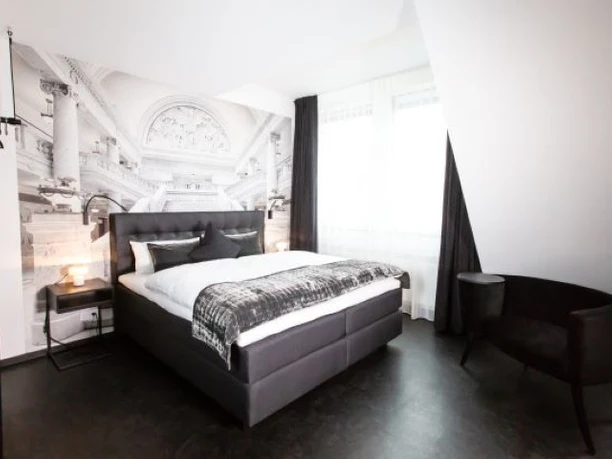 Boutique Hotel K7 - Modernes Hotelzimmer Modernes Hotelzimmer in Schwarz-Weiß mit einem Boxspringbett, einer imposanten Fototapete mit Architekturmotiv und einem schwarzen Samtsessel.