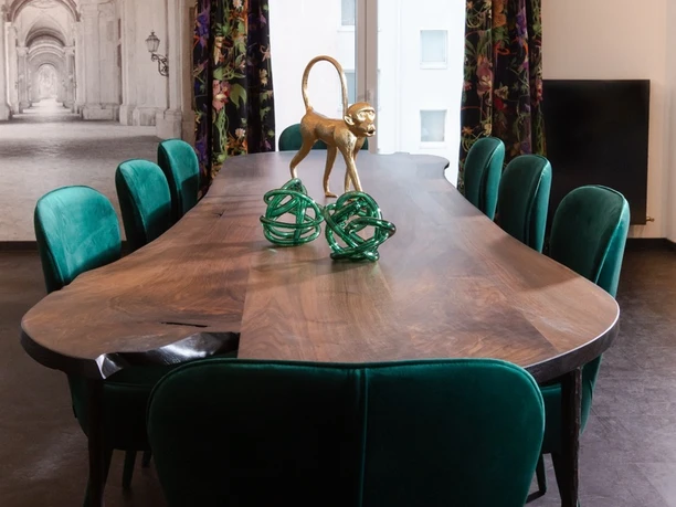 Boutique Hotel K7 - Conference table An elegant solid wood conference table with wavy edges, surrounded by emerald green velvet chairs under a classic chandelier.