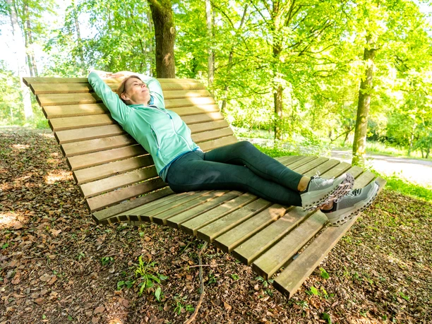 Bad Driburg-Buddenberg Arboretum-Teutoburger-Wald-Bad-Driburger-Touristik-GmbH-D-Ketz-053.jpg Frau entspannt auf geschwungener Holzliege im Buddenberg Arboretum zwischen Bäumen.