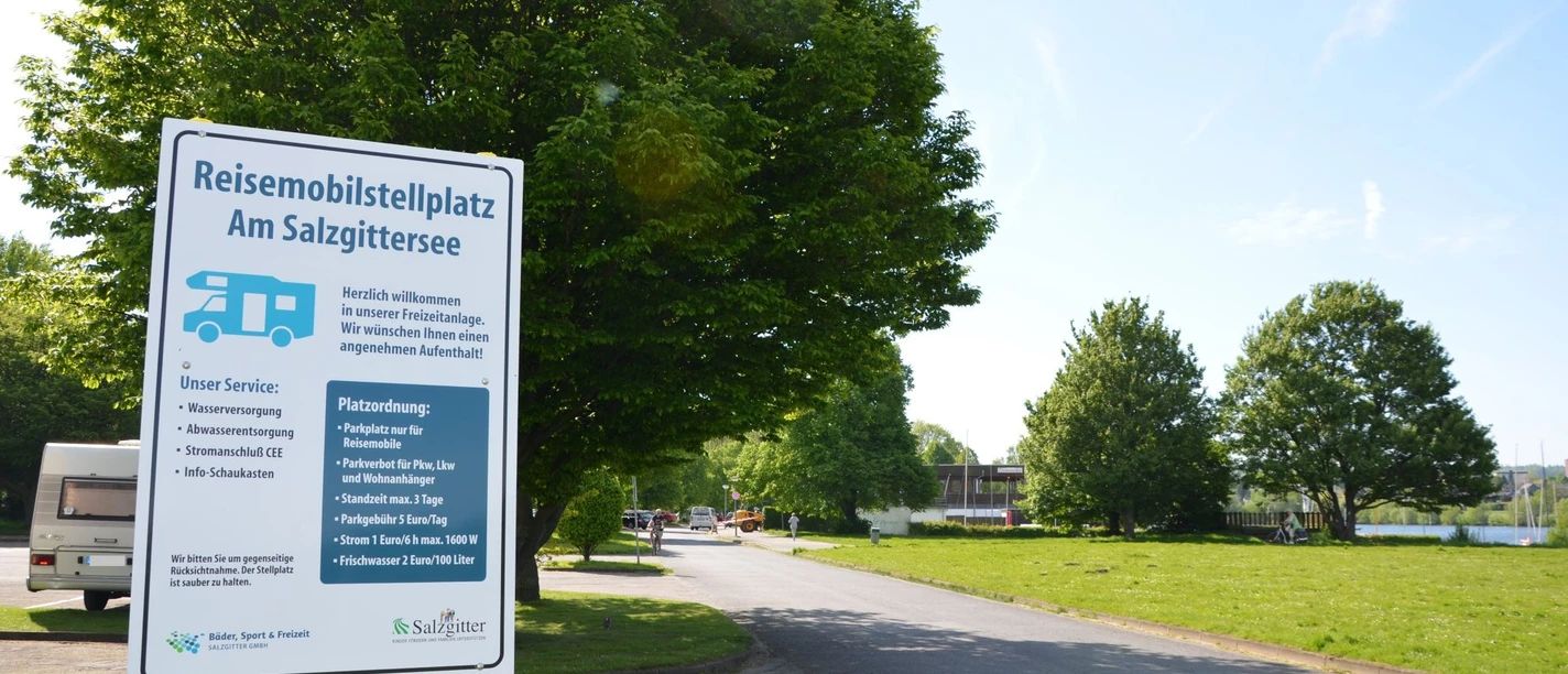 Wohnmobilstellplatz_Salzgittersee_HD_16zu9.JPG Weißes Hinweisschild für den Reisemobilstellplatz am Salzgittersee an einer Zufahrtsstraße.