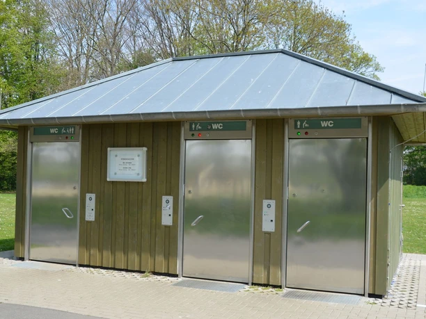 Toilettenanlage_Piratenspielplatz_HD_16zu9.JPG Öffentliche, barrierefreie WC-Anlage am Piratenspielplatz mit Holzverkleidung und Edelstahltüren.