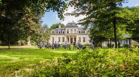 Fahrradfahrer vor dem Palais Radfahrer pausieren vor einem herrschaftlichen weißen Gebäude, umgeben von einem großen Park.