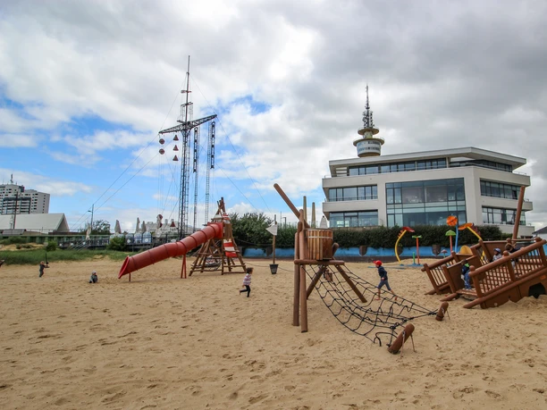 Spielplatz Weser-Strandbad IMG_4864_WEB.jpg Strandspielplatz mit Holzschiff, Rutsche und spielenden Kindern im Sand des Weser-Strandbads.