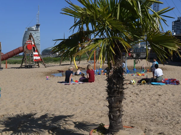 Spielplatz Weser-Strandbad DSC_0732 (c) Wolfhard Scheer_Erlebnis Bremerhaven_WEB.jpg Palme im Sand vor Familien am Wasserspielplatz und dem Hotel Sail City.
