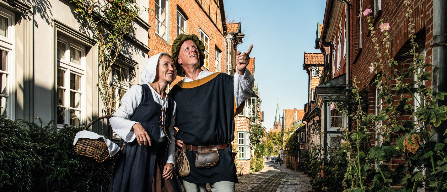 Claas und Trine_CC_BY-SA_(C)Lüneburg Marketing GmbH_BorowiakZiehe.jpg Historisch gekleidete Gästeführer in der westlichen Altstadt. Der Mann zeigt nach oben.