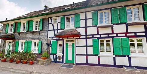 Ferienwohnung Haan Fachwerkhaus von außen, mit grünen Fensterläden und Blumen vor der Tür.
